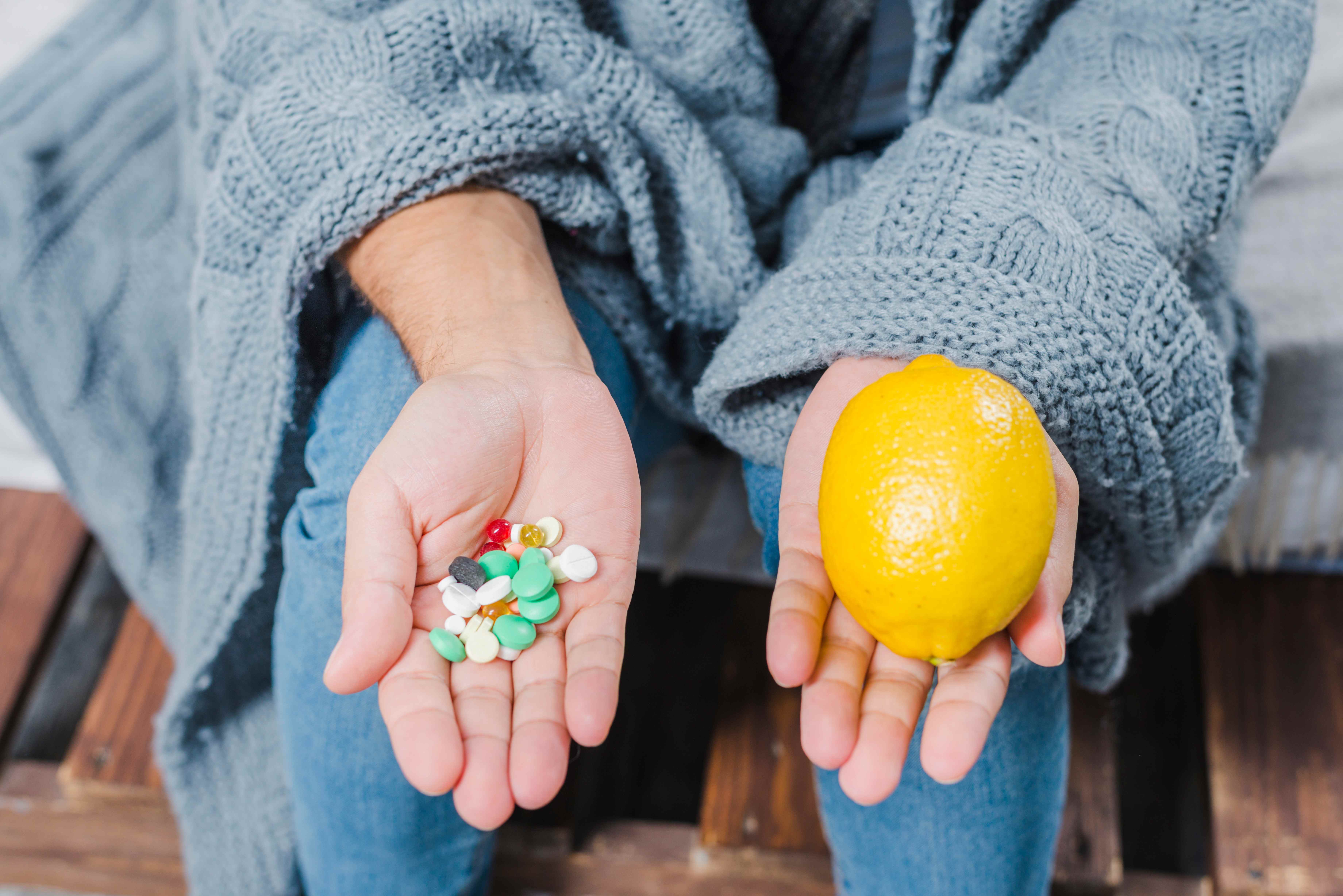 Person holding vitamin supplements in one hand and a fresh lemon in the other